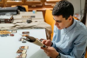Jovem profissional lendo revista com cards colecionáveis sobre a mesa do seu home office com decoração geek.
