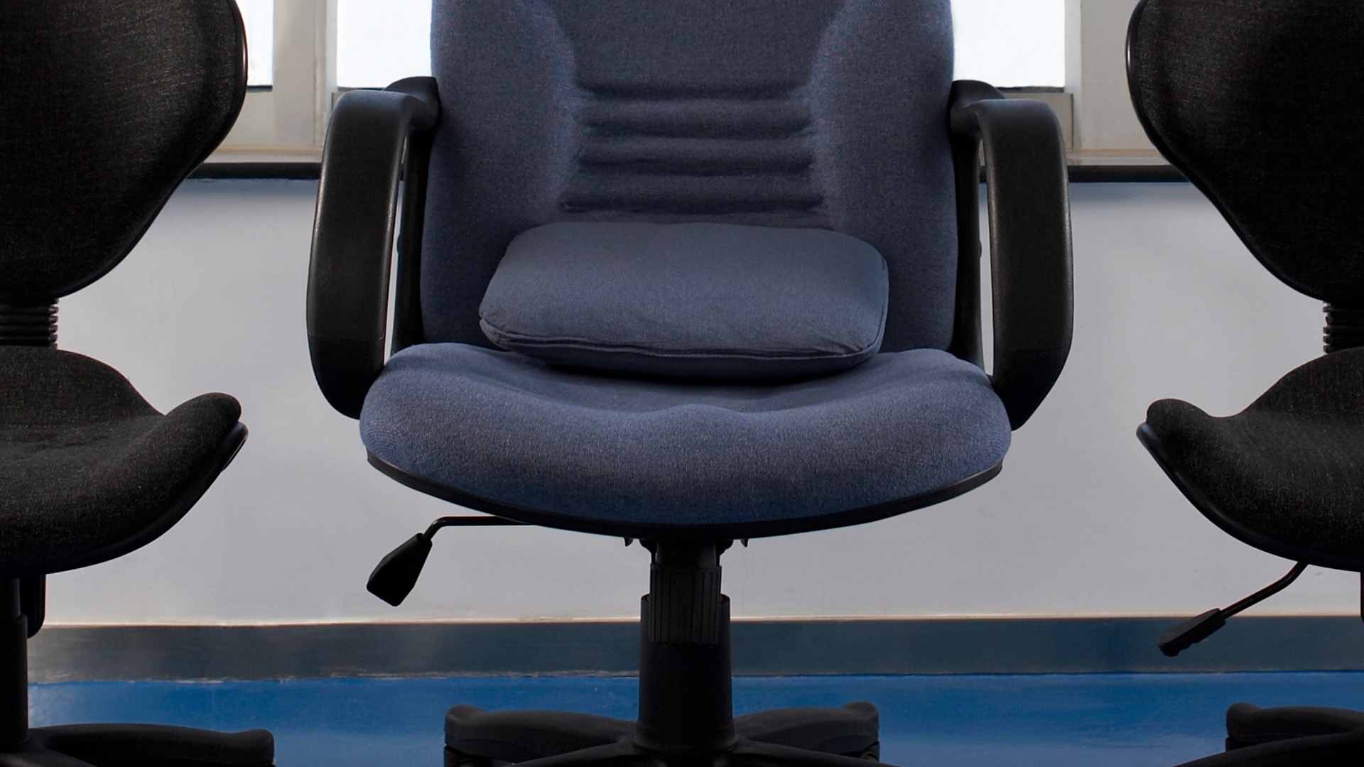 uma cadeira de escritório preta com um almofada improvisando o suporte de lombar