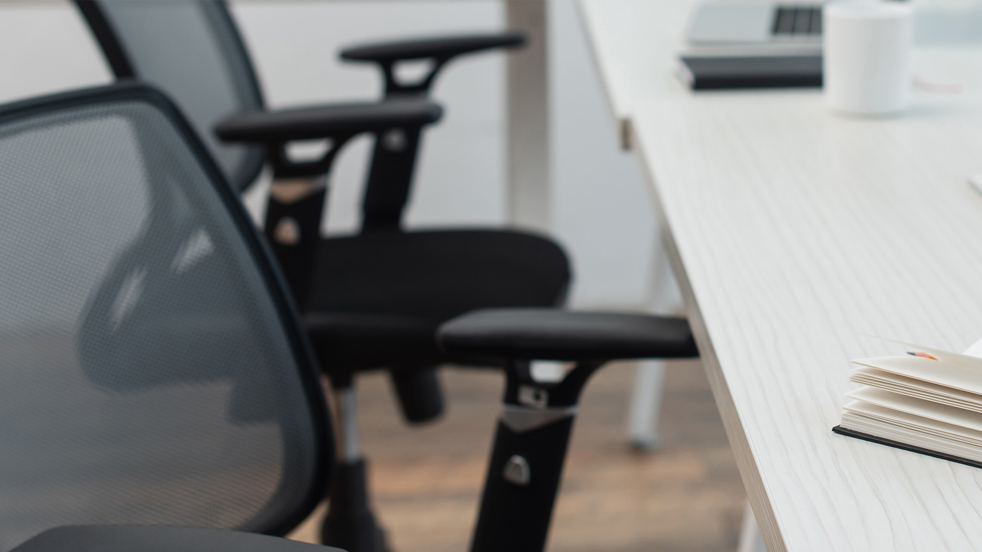imagem com duas cadeira de escritório convencionais, em frente a uma mesa de escritório branca, imagem do artigo cadeiras ergonômicas do blog slikdesk