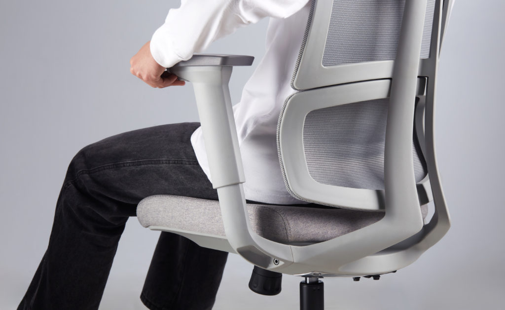 detalhe do apoio de braço 3D da cadeira ergonomica slikdesk ergo, modelo com camiseta branca e caixa jeasn preta sentado na cadeira cinza claro enquanto ajusta o apoio de braço