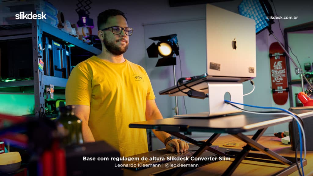 foto do leonardo kleemann @leokleemann em pé, com uma camiseta amarela em seu estudio de gravação, em pé utilizando seu notebook em cima de uma base com regulagem de altura converter slim da slikdesk